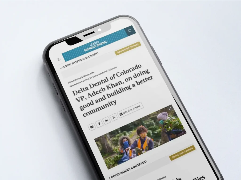 A phone with an article pulled up titled "Delta Dental of Colorado VP, Adeeb Khan, on doing good and building a better community"