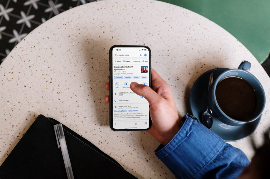 A hand holding a phone that displays a google search for Crossing Pointe North Apartments