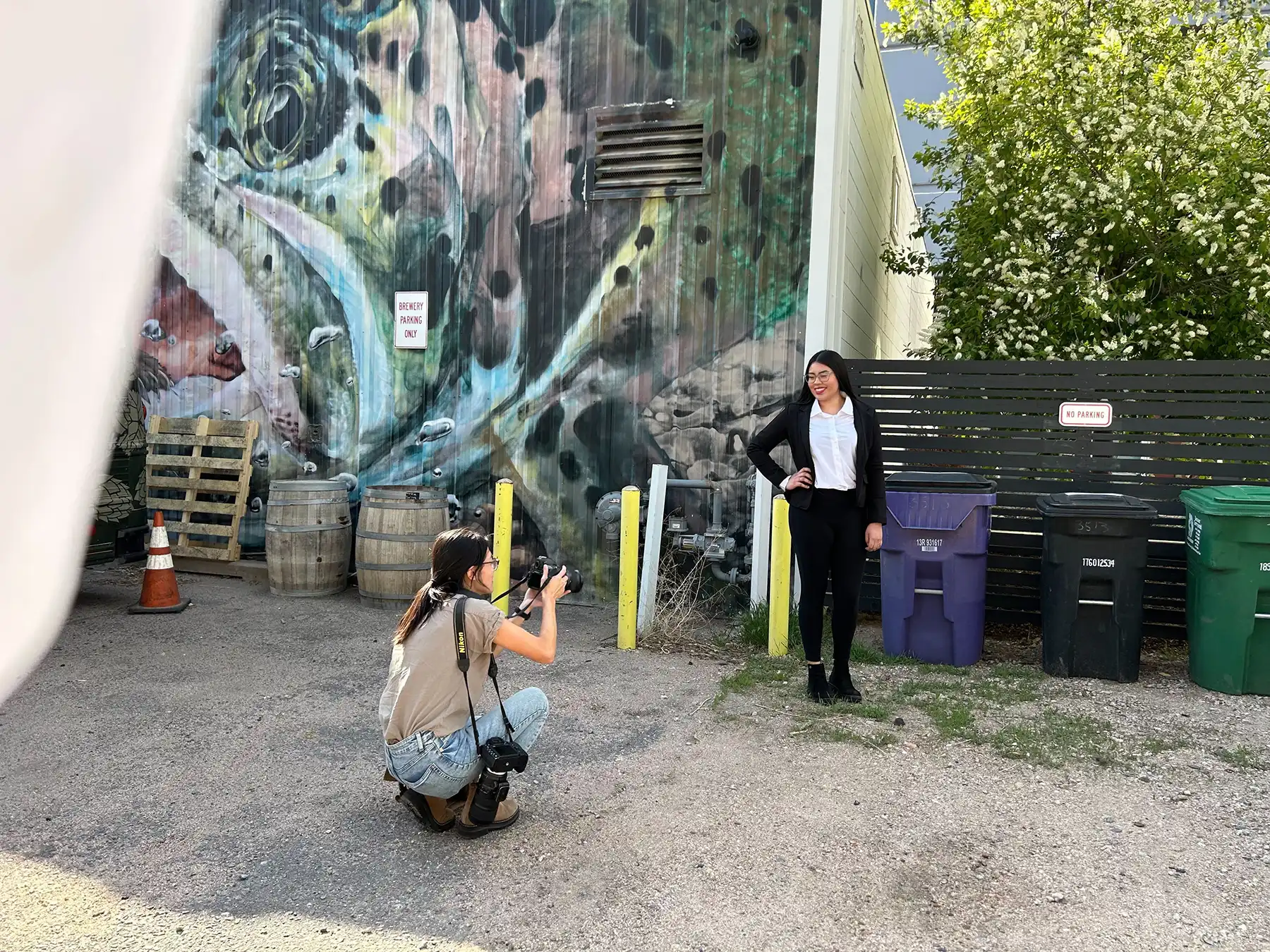 A photographer kneels down to take a picture of dental student Paola Hernandez in front of a wall with a street painting of a fish.