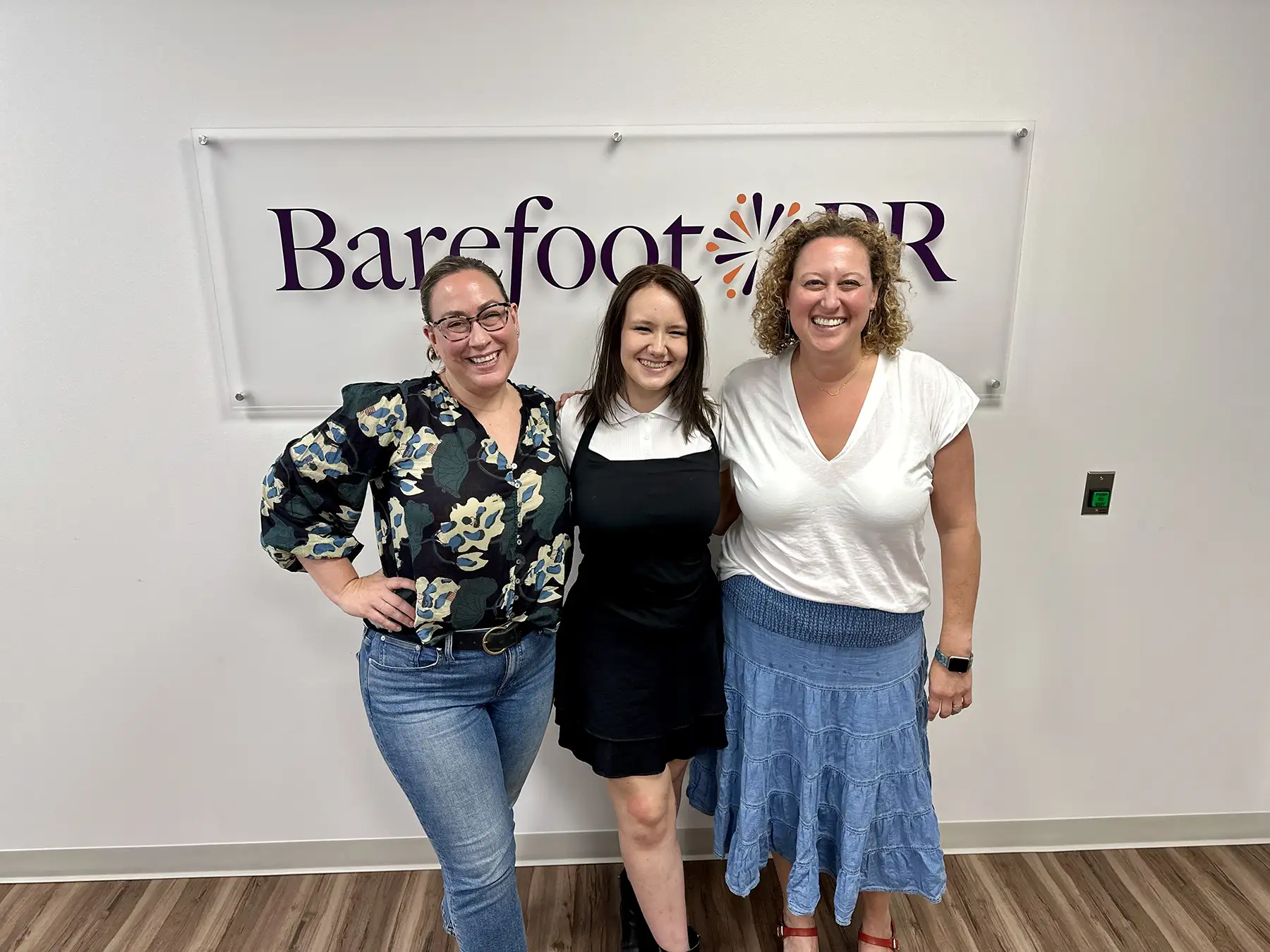 Kass with Cori and Sarah in front of the Barefoot PR sign in the office.