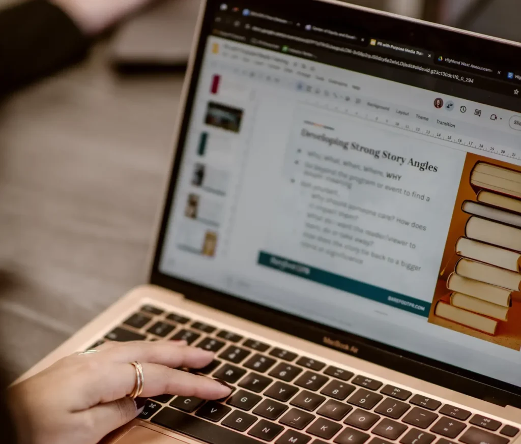 A woman types on a laptop with a presentation about story angles on the screen.