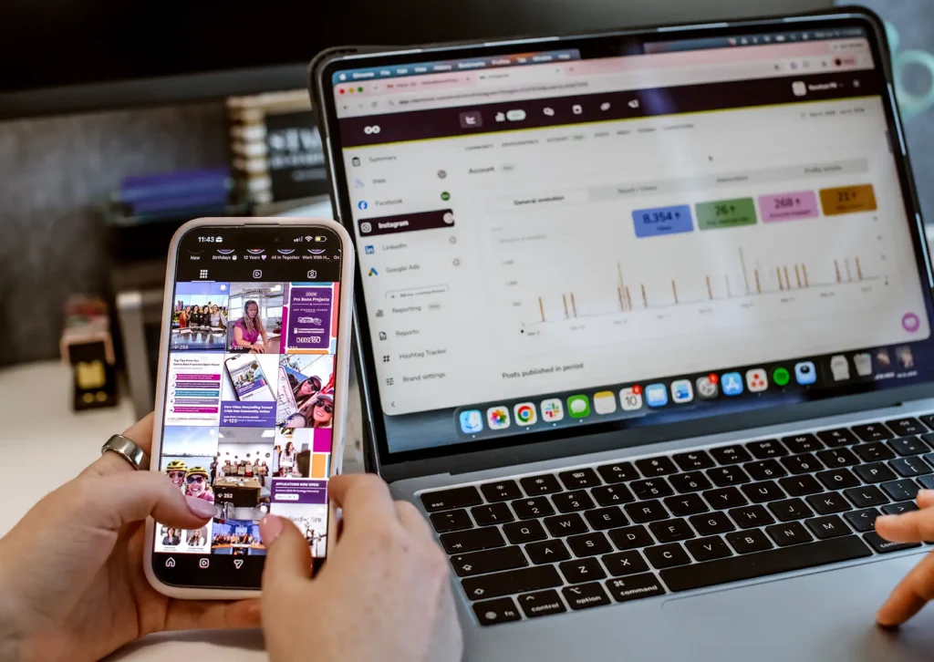 A phone showing a social media feed and a computer with metrics in the background