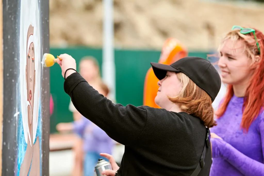 2 women paint a mural on a wall using spray paint