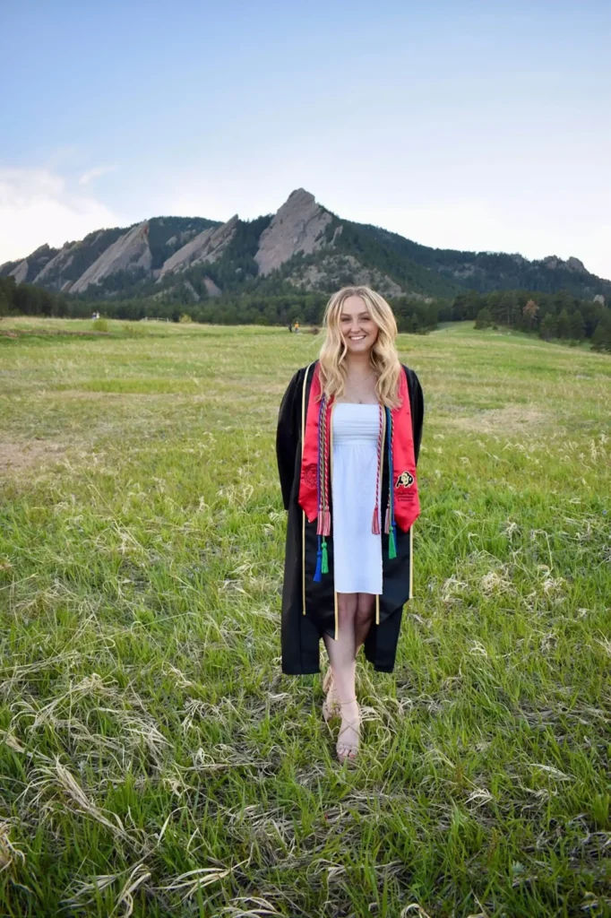 Emily in her CU Boulder graduation gown and stoles in front of the flatirons